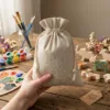 Lněné pytlíky držené v ruce na pozadí výtvarných potřeb a kreativních pomůcek