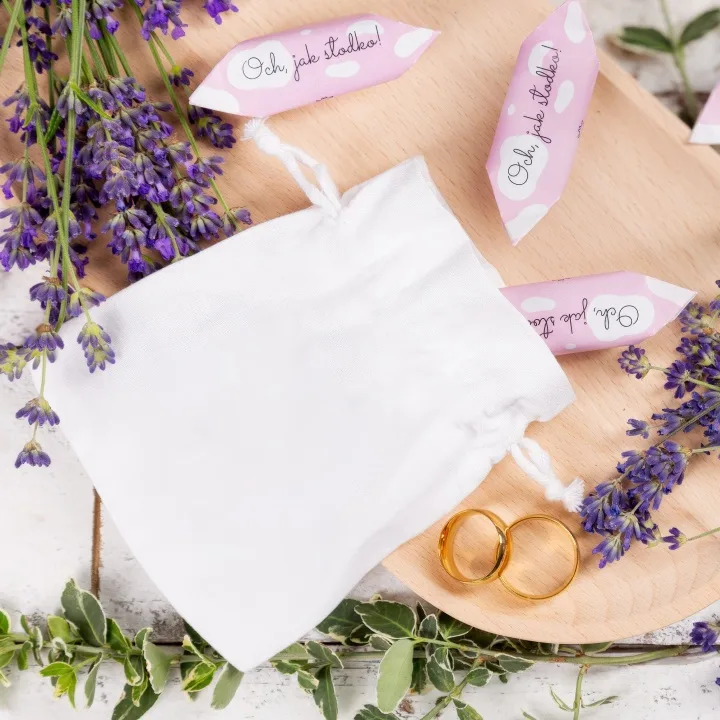 Elegantní bílý saténový pytlík u zlatých svatebních prstýnků a levandule.